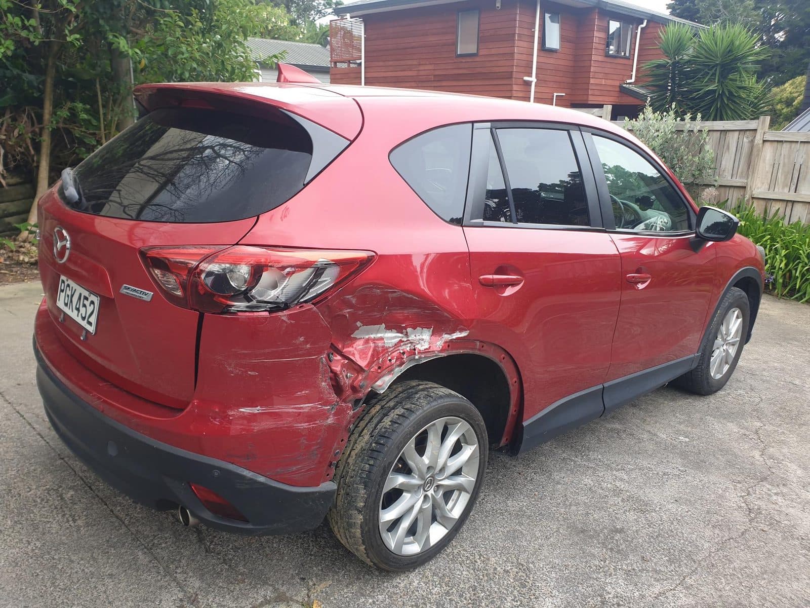 Dented rear quarter panel and scraped bumper on a red Mazda CX-5 before repair