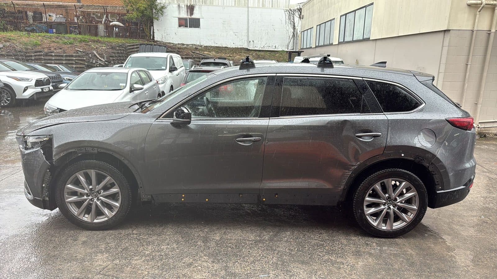 Torn front bumper and broken lights on a grey Mazda CX-9 before repair